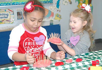 Braelynn Atkins, left, and Colette Holland, both 5 years old and both from Stewartville, made pretend birthday cakes out of red Playdough and topped them with pretend candles (toothpicks) to celebrate Valentine's Day at the Wee Care Learning Center last Thursday, Feb. 13.  Above, Colette presents her cake and happy birthday wishes to Braelynn.