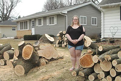 Teresa Jorgenson stands near three large piles of logs at her home at the 200 block of Fifth Avenue Southeast last week. The logs are the remains of a huge tree that stood at the property for many years. Tree removal companies hired by People's Energy Cooperative trimmed or removed a number a trees along the street last week. Sean Hale, public works director for the city of Stewartville, said People's Energy wants the trees trimmed so the branches don't interfere with nearby power lines. If the tree trimming makes a tree look odd, some residents may decide to remove the tree entirely, Hale said. City crews have also removed 20 to 30 ash trees, victims of the emerald ash borer, on public property since last fall, he said