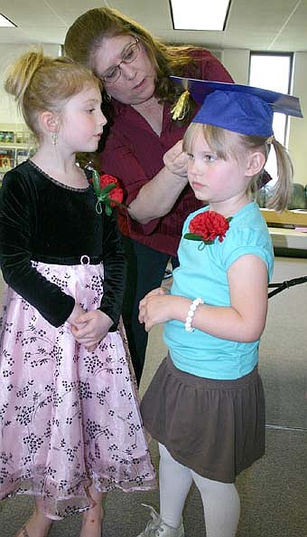 Sixty-two children concluded their time at St. John's Wee Care with a graduation ceremony at St. John's Lutheran Church on Sunday, May 4. Here, Lori Torgerson, a Wee Care teacher, helps Ashlee Voshart, right, with her mortarboard as Cydney VanTassel looks on. 