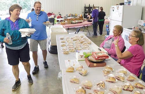 Deb and Jeff Goeldi of Racine, left, walk near the pie table at the annual Racine Lions Club Chicken Feed at Racine City Hall on Saturday, July 20. DeeAnn Byrne and Maxine Vrieze of the Racine Methodist Church, right, sold many flavors of pie for $2 per slice.