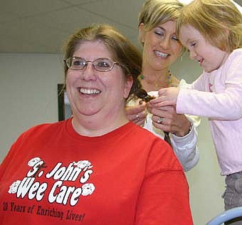A HAIRCUT -- Lori Torgerson, a teacher at St. John's Wee Care, sits still as Daesha Emmons and her 4-year-old daughter Jaida  work to remove two 10-inch braids of hair at Wee Care last week. 