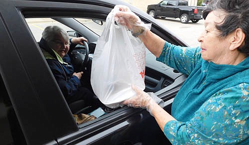 Sharon McAtee, site coordinator for the Center for Active Adults, right, delivers a Gleason's-cooked meal to Pat Leonard, left, just outside the Center's front door on Wednesday, April 29. Due to concerns about the spread of the coronavirus, the Center's members and visitors no longer eat their weekday lunches together. However, the curbside pickup has been popular, with 40 to 60 seniors stopping by the Center each weekday.