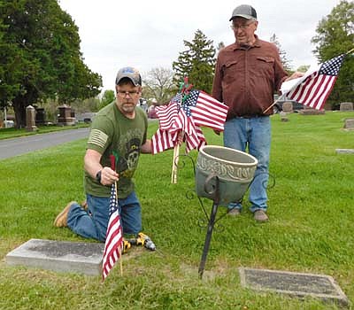 Troy Helget, commander of Stewartville VFW Post 8980, with American Legion member Dean Ramaker looking on, places a flag at the grave of Henry Gathje, a private in the U.S. Army during World War II, on May 22.
