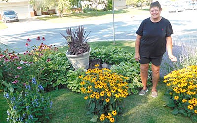 Peg Paulson stands with her garden near the intersection of Third Avenue Northeast and Fourth Street Northeast. She said she enjoys spending time with her flowers and plants , which include black-eyed Susans, Russian sage, coneflowers and hostas. She says she tends to her  garden about 15 hours a week. "I enjoy putzing and digging, and making things look nice,"&#8200;she said. ""It's relaxing. It's good therapy. I get a lot of nice compliments."