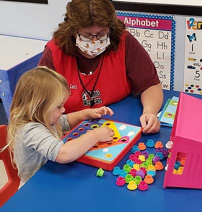 While wearing her bee-themed face mask, Lori Torgerson, caterpillar teacher, left, helps Wee Care student Harbor Lawrence play a fun game.