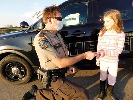 Nora Picker, 8, a second grader at the Central Education Center, accepts a sticker from Jason Owen, Stewartville's community oriented policing (COPS)&#8200;deputy, at a National Night Out party on Tuesday evening, Oct. 6.