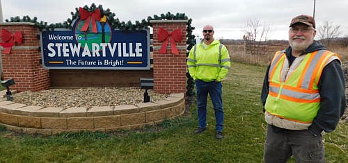 Members of the city of Stewartville's public works department, including Scott Priebe, foreground, and Eric Domino, have decorated the city's entrance signs in festive red and green for the coming Thanksgiving and Christmas seasons. Here, Priebe and Domino pose near the sign along County Road 6 about two miles west of Stewartville.