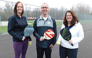 PLEASED PICKLEBALL PLAYERS -- From left, Amy Koenigs, Kevin Koenigs and Kari Koenigs pose with their pickleball paddles at the Bear Cave Park tennis courts, where the city of Stewartville plans to convert one of the four tennis courts into two pickleball courts. "We're very excited that we'll actually have a true (pickleball) court," Kari said.