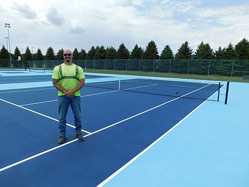 Eric Domino, public works employee, poses at a recently resurfaced tennis court now ready for play at Bear Cave Park. A portion of two new pickle ball courts and a basketball court can be seen in the background. Domino and Scott Priebe, another public works employee, placed the nets at the courts last week.