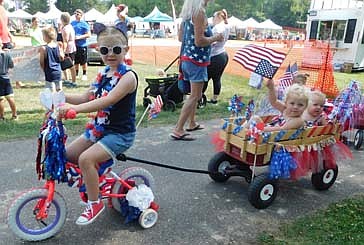 Aubrie Ristau, 5, of Stewartville, rides a decorated bicycle pulling a wagon carrying Ava Doll, 1, in back, and her sister Charlotte, 2, who waves an American flag to celebrate Independence Day during the Summerfest Kids Parade at Bear Cave Park on Sunday, July 4.