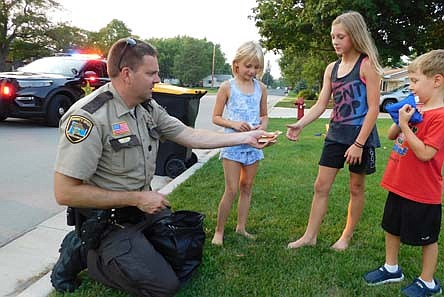 Jason Owen, Stewartville's community oriented policing (COPS)&#8200;deputy, left, hands out Frisbees, pens and Olmsted County Junior Sheriff stickers to the children at a National Night Out celebration at the home of party host Jenny Anderson at the 400 block of Fourth Avenue Southeast on Tuesday evening, Aug. 3. Kids welcoming Owen to the neighborhood include, from left, Hope Anderson, a third grader to-be at Bear Cave Intermediate School; Brystol Schmidt, who will be a sixth grader at Stewartville Middle School; and Kelby Steichen, who will be a kindergartner at Bonner Elementary School this fall.