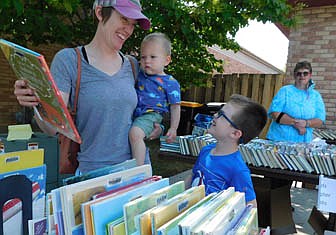 Kathryn Yetter, left, holding her 1 1/2 year-old son William as she smiles at her 6-year-old son Logan, is one of many Stewartville and area residents who bought books from the Stewartville Public Library for 50 cents each at the Library's Book Sale, held on Wednesday, Aug. 18 and Thursday, Aug. 19. Yetter enjoyed browsing for books. "I'm pretty excited," she said. "There are so many books here, and everybody benefits from a book sale." Sue Edge, library associate who assisted with the sale, looks on in the background.