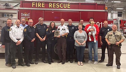 Kevin Torgerson, Olmsted County Sheriff, center, presented a life-saving award to the Stewartville Fire Department last week, thanking the firefighters for helping save the life of Logan Olson of Stewartville, who was 18 months old when he fell into a retention pond near the 700 block of Willow Green Court Northeast in Stewartville on Wednesday, April 7. Logan was rescued by his dad, Darwin (DJ), his babysitter, and several passersby who helped administer CPR. Shortly thereafter, Stewartville's first responders arrived, taking over the rescue efforts. Logan, taken to St. Marys Hospital in critical condition, remained hospitalized nearly two weeks before returning home on April 19. DJ Olson, third from right, holds Logan as he is joined by his wife, Erin Olson,fourth from right. First responders who helped save Logan include, from left, Aaron Jones, Steve Wolf, Greg House, Jim Elliott, Steve Denny, Lisa Jelinek, (Sheriff Torgerson), Justin Lonien, Dan Swanson and Ben Wolf. Sgt. Nick Jacobson of the Olmsted County Sheriff's Office, standing at far right, in charge of patrol staff on April 7, nominated Stewartville's first responders for the award.