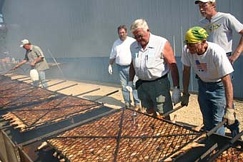 COOKING THE CHICKEN -- Dennis Graff, far right, and Don Lyman, standing next to Graff, both of the Racine Lions Club,  prepare to turn the chicken at the club's annual chicken feed at the new Racine City Hall on Saturday, July 21.  Lions Club members prepared 700 chicken halves, Lyman said.   