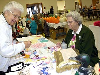 LOOKING THINGS OVER -- Eleanor House of Stewartville, above left, looks at crocheted items, cloth loons and towels made by Marilyn Nord, right,  at the senior citizens craft show and bake sale at the Stewartville Civic Center on Saturday,  Oct. 13. 