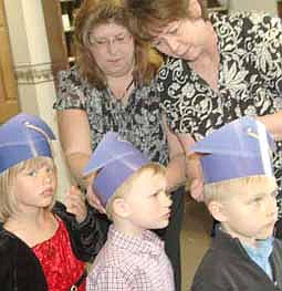 Wee Care celebrated its annual graduation at St. John's Lutheran Church on Sunday, May 6. Here, Lori Torgerson, Wee Care teacher, left; and Becky Case, assistant teacher, help students with their graduation hats, including, from left, Maddie Kath, Zach Green and Carter Dick. 