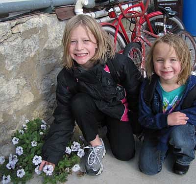 Bailee Swanson, a fourth-grader at Central Intermediate School, left, and Jacie Dudley, a kindergartner at Central, kneel near the flowers that continue to grow along the base of the old Tews Hotel building in downtown Stewartville. Brian Ferson, owner of the building, said he was amazed that the flowers are still growing despite the below-freezing temperatures at night. Ferson said that the flowers remind him of Jesus's parable about seeds being planted in good soil. "Those seeds found a little bit of good soil," he said. 