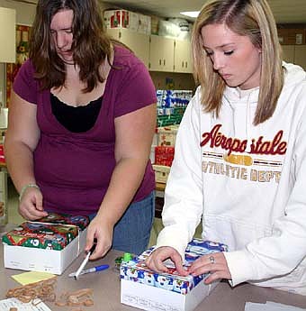WORKING FOR THE POOR -- Amanda Eggert, a senior, above at left, and Erica Nelson, a junior, right, put tags on boxes filled with items such as hygiene enhancers, toys, school supplies and hard candy. Students have a goal of completing 622 boxes. In the photo at left,  Coty Bredesen, a junior, prepares more boxes. 
