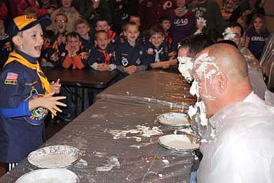 Cub Scout, Ian Reese, shows his excitement after landing a cream pie in the face of his leader, Ryan Colligan, as other scouts watch and cheer! Other Wolf den leaders pictured are Dana Halferty (front) and Scott Boelman (back).  