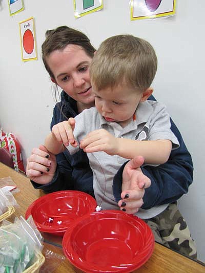 Parker Carrigan, 2 1/2, of Stewartville, focuses intently on placing beads on a string as he makes ornaments at the SECFE Holiday Fun Night at the Early Childhood Learning Center last Thursday evening, Dec. 13. Kelly Carrigan, Parker's mother, lends a hand. Parker is a student in a  SECFE parent-child class. 
