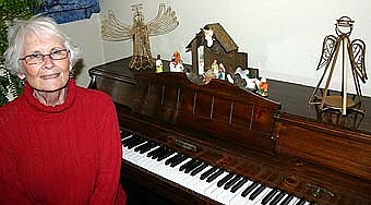 READY FOR CHRISTMAS -- Connie Hayes sits near the piano at her home at 102 Lakeshore Drive.  The house is adorned for Christmas, as evidenced by the two angels and the Nativity scene atop the piano.  Helen Tews Hagen, the daughter of the owners of the Tews Hotel, once lived in the home. Mrs. Hagen's quality choices for wall coverings and other furnishings remain evident. 