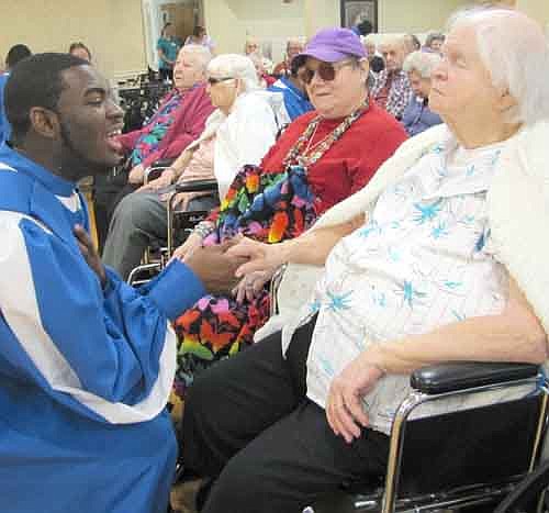 A member of the Rust College A'Cappella Choir pauses to shake hands with Bea Raygor, a resident of the Stewartville Care Center, as the choir sings "I'll Meet You in the Morning" at the Care Center last Tuesday morning,  April 23.
