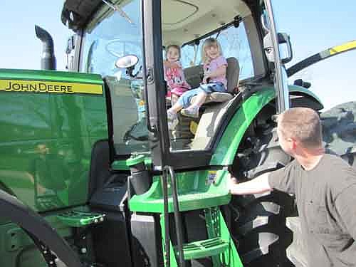 Katie Nelson, at left above, and Clara Henderson, students at Stewartville's Wee Care, sit high atop the seats in a John Deere tractor in the Wee Care parking lot on Tuesday, May 7. Kyle Hinkle, father of Wee Care student Keely Hinkle, stands in the foreground at right. Hinkle brought the tractor to Wee Care to answer the children's questions about farming and tractors.
