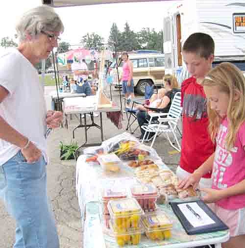 Hunter Olson, 10, and his sister Karley, 8, of Stewartville, sold a number of items from their garden at home, including tomatoes, squash and peas, at Stewartville's Farmers Market last week. Pam Carolan of Stewartville, left, appears ready to make a purchase.