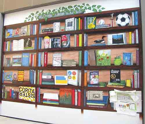 Peter Lex, a 1987 graduate of Stewartville High School, right, has transformed a garage door at the Rochester Public Library into a painting of a finely detailed, vivid bookshelf.