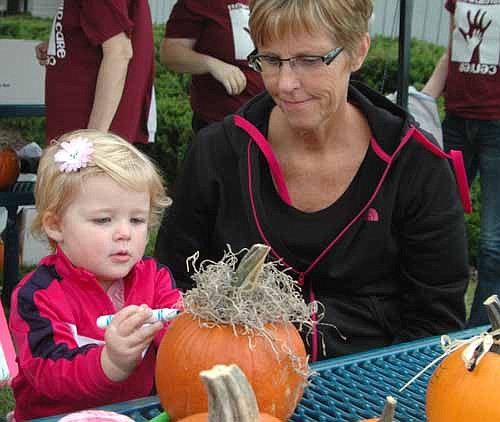 Aubrey Thompson, 23 months, of Chatfield, focuses on decorating a pumpkin under the watchful eye of her grandmother, Kathy Sowers of Racine, at the Stewartville Morning Lions Club's annual Fall Festival at the parking lot north of  Stewartville City Hall on Saturday, Sept. 28. "We came to help the kids have a fun day, do some activities and check out the Fall Festival," Sowers said.