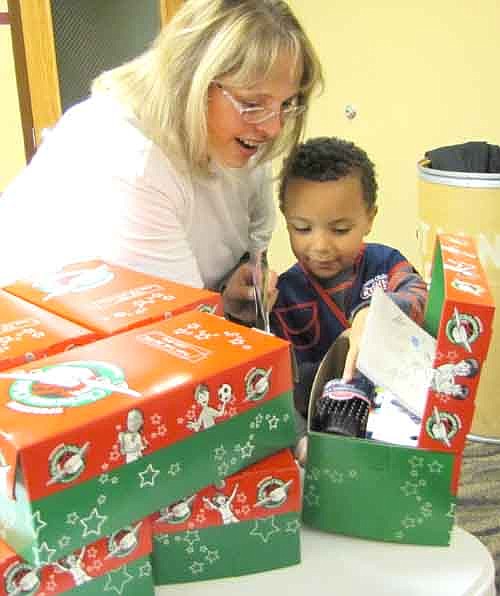 Kimberly Alwin, coordinator of Operation Christmas Child at Grace Evangelical Free Church, helps Kaydn Davis, 3, of Stewartville, above, look through the contents of a box that will soon be sent to a poor child across the world.