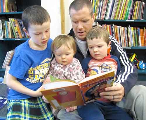 Andrew Langseth of Stewartville reads a book about wrestling to three of his children, including, from left, Josh, 7; Reagan, 1; and Asher, 4, at the Stewartville Public Library's Wee Care Pajama Night last Thursday, March 13. Many Wee Care parents and their children attended the event. Asher Langseth is a student in a butterfly class at Wee Care.