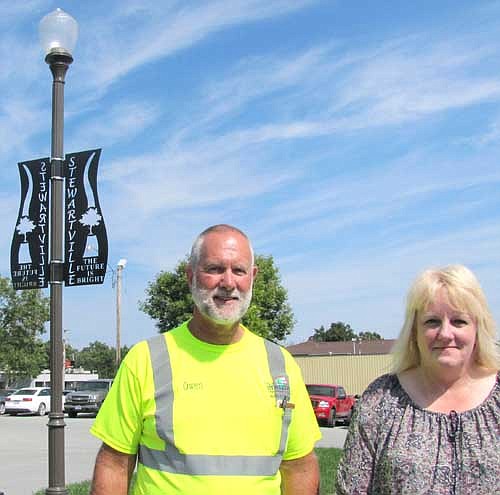 Owen Sass, public works supervisor, left, and Laurel Jacobs, city receptionist and data clerk, stand near the new signs at the grass-covered island at the City Hall parking lot.