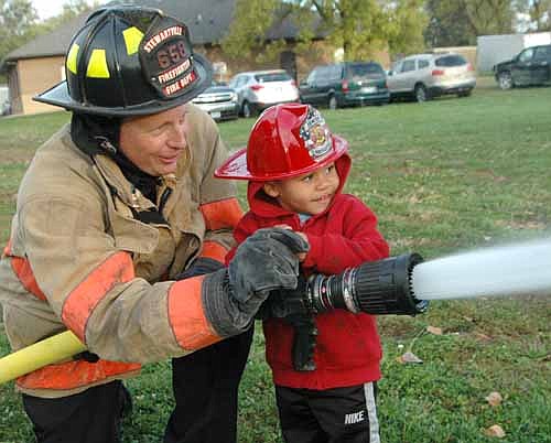 Treydon Logan, 2 1/2, of Stewartville, guided by firefighter Aaron Jones, uses a fire hose at the Stewartville Fire Department's annual open house last Wednesday, Oct. 8. Hundreds of children and their parents saw the SFD's new Fire Hall.