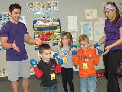 Jameson Hanson, a personal training manager, left, and Megan Mullenbach, a personal trainer, both with Anytime Fitness, supervise as three kindergartners, including, from left, Joel Dominguez, Hailey Hatz and Aidyn Voyna, work out with weights.