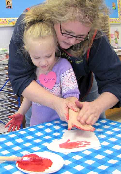 Sandy Steinhoff, a teacher at Wee Care at St. John's Lutheran Church, helps student Emma Rahlf apply a painted hand to a paper heart for a Valentine's Day art project at Wee Care on Thursday, Feb. 12.