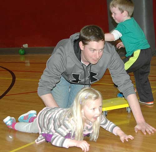 Tyler Carrigan, one of many dads who attended the "Daddy and Me Gym and Pizza Night" at Central Interme-diate School, helps Ava Bowler go for a ride on a wheeled cart in the school's gym last Thursday, March 19. Graham Carrigan, Tyler's son, stands in the background.