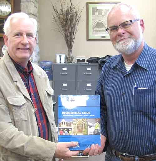 Chuck Willihnganz, Stewartville's building inspector, left, presents an updated Minnesota Building Code book to Les Radcliffe of Radcliffe Homes during last week's City Council meeting. Southern Hills (Sun Communities) and Smidt Companies of Racine also won new Building Code books in a drawing held to celebrate May as Building Safety Month.