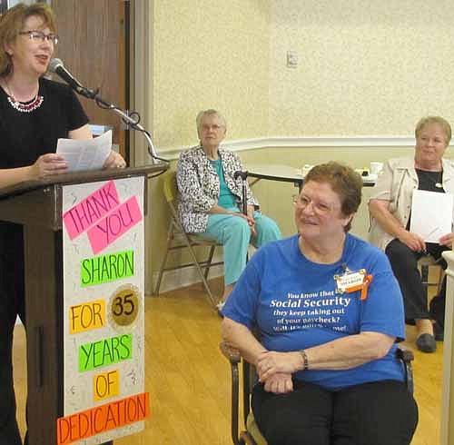 Suz Eberle, activities director at Root River Estates and the Stewartvilla Apartments,  standing at left, pays tribute to Sharon Bernard, seated in foreground, at a party in Bernard's honor at the Care Center on Wednesday, May 27. Bernard has announced her retirement after serving as the activities director at the Care Center for 35 years.