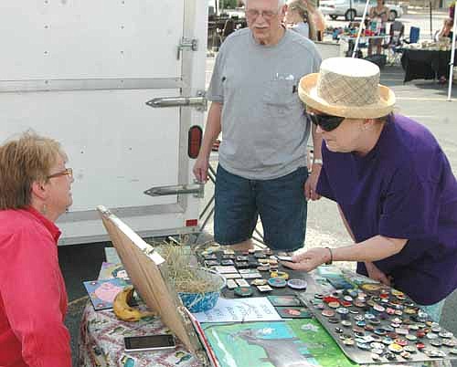 Betty Butters of rural Stewartville, left, sold eggs, buttons, paintings and magnets made out of old jewelry at the Stewartville Area Chamber of Commerce's  Tuesdays off Main Farmers Market in downtown Stewartville last Tuesday, June 9.  Dale and Janne Kangas of Stewartville, right, took a few moments to look over the items at Butters's booth.