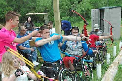 Stuart Olsen of Seattle, Washington eyes the target during archery practice at the National Wheelchair Sports Camp. Micah Ostergard, a member of the summer staff at Ironwood Springs Christian Ranch, far left, provides Olson with a pointer or two.
