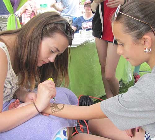 Kayley Dahle, a henna artist, left, draws a heart of the forearm of Summer Barber, 11, who will be a sixth grader at Stewartville Middle School this fall.