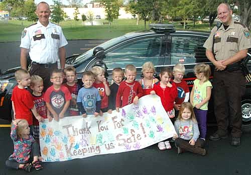 Olmsted County Sheriff Kevin Torgerson, standing at left, and Zak Breitenbach, Stewartville's community oriented policing (COPS) deputy, standing at right, visited the children at St. John's Wee Care on Monday morning, Sept. 21. The children displayed a poster thanking the officers for their work to keep the community safe.