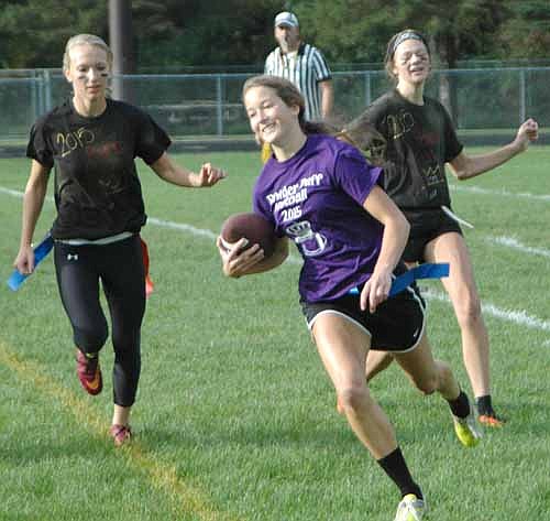 Senior running back Mariah Terhaar eludes the pursuit of junior defenders Kallie Keller (left) and Olivia Waltman during the homecoming powder puff football game.