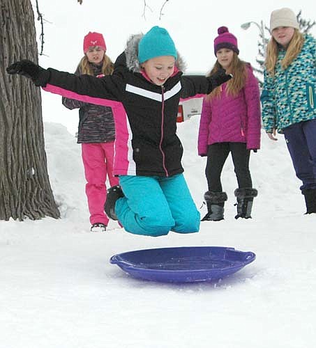 Anneliese St. Martin, a fourth grader, flies through the air and prepares to land on a saucer and head down the hill. Looking on in the background, from left, are fourth graders Megan Myhrvold, Cami Hoth and Anna Cummins.