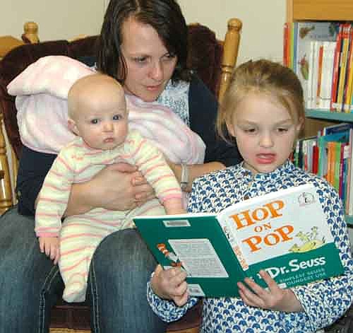 Kaysie Manion of Stewartville holds 6-month-old McKinnley and listens to daughter Morgyn, 7, read Hop on Pop by Dr. Seuss at the annual Pajama Party for St. John's Wee Care students and their parents at the Stewartville Public Library last Tuesday evening, March 8.