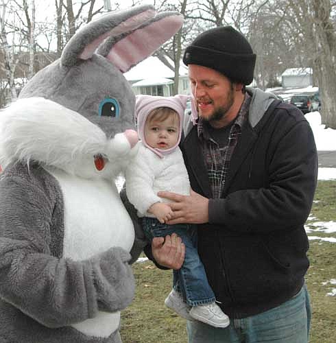 Kathryn Rundle, 15 months, held by her dad Mark, of rural Stewartville, meets the Easter Bunny at the Stewartville Sons of the American Legion Easter Egg Hunt on Saturday morning, March 26. About 80 children, accompanied by their parents, took part in the proceedings at Florence Park.