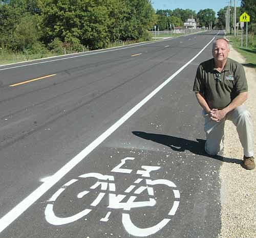 Bill Schimmel Jr., city administrator, kneels near the new bicycling/walking lane along the east side of Sixth Avenue Southwest. Responding to safety concerns, the Stewartville City Council has prohibited parking along both sides of the road.