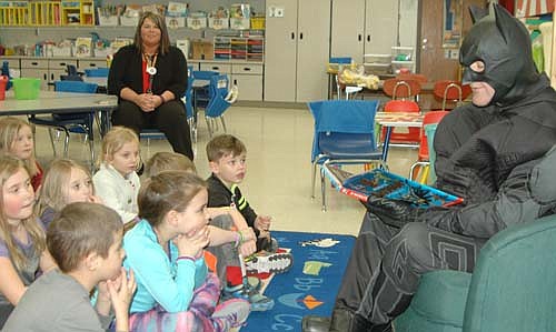 Batman, portrayed by Rob Mathias, the chairman of the Stewartville School Board, read a book detailing the history of the Caped Crusader to a kindergarten class at Bonner Elementary School last Thursday, Feb. 23. Lindsay Dick, the children's teacher, listens in the background.