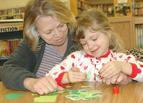 Children from St. John's Wee Care wore pajamas to separate gatherings at the Stewartville Public Library on Monday, March 6 and Tuesday, March 7. Parents and grandparents read to the Wee Care students or helped them make shamrocks. At left, Valerie Kafka of Stewartville assists as her granddaughter, Kira Kafka, 5, a Wee Care butterfly student, adds glue to a shamrock leaf on Tuesday evening, March 7.